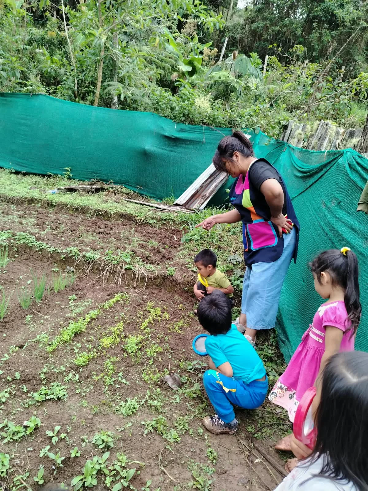 Maestra acompañando a los niños mientras exploran el huerto con lupas